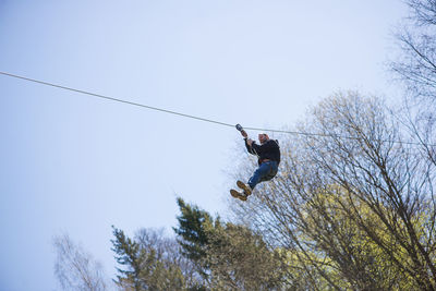 Low angle view of man zip lining against clear sky