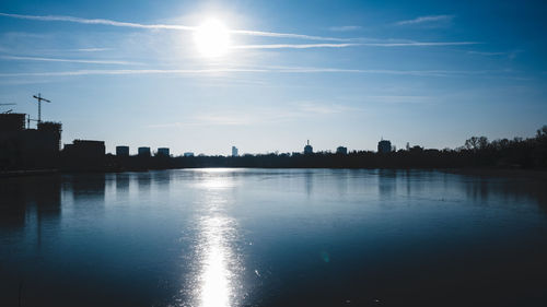 Silhouette buildings by river against sky