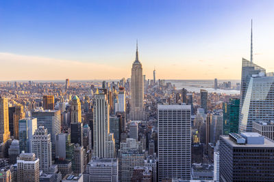 Empire state building amidst cityscape at manhattan during sunset