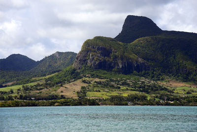 Scenic view of sea by mountain against sky