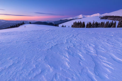 Snow covered landscape against sky during sunset