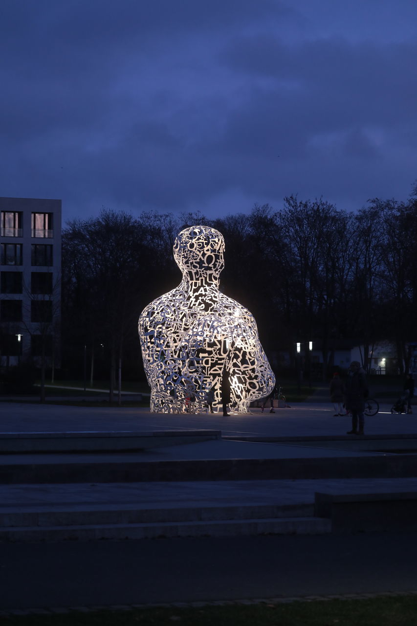 STATUE BY ILLUMINATED BUILDING AGAINST SKY AT DUSK