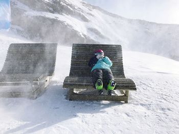 Full length of woman wearing warm clothing while lying on seat at snowcapped mountain