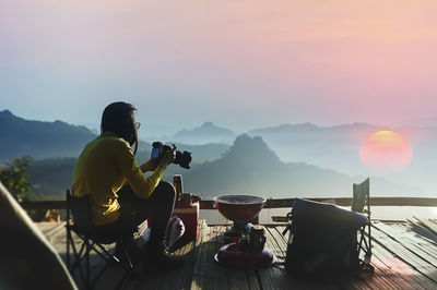Man sitting on mountain against sky during sunset