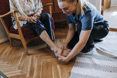 Female caregiver helping senior woman to wear socks at home