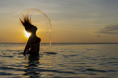 Woman in sea against sky during sunset