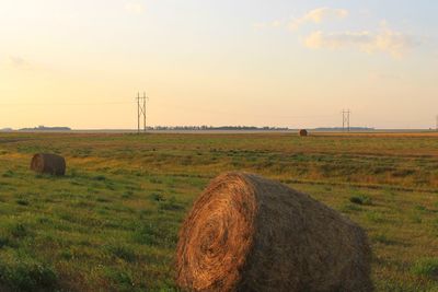 Hay bales on field against sky during sunset