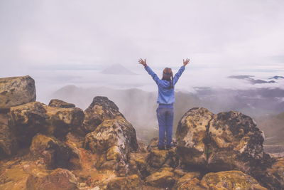 Young woman standing on rock formation against sky