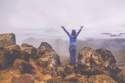 Rear view of woman standing on rock against sky