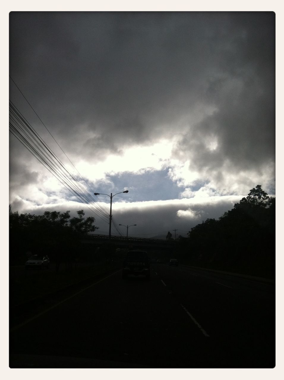 sky, transportation, transfer print, road, cloud - sky, car, cloudy, road marking, the way forward, tree, auto post production filter, cloud, street, land vehicle, diminishing perspective, mode of transport, country road, silhouette, overcast, nature