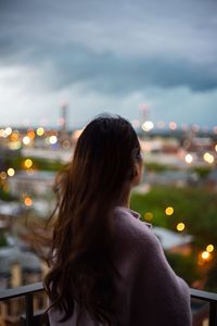 Rear view of woman standing in balcony against cloudy sky at dusk