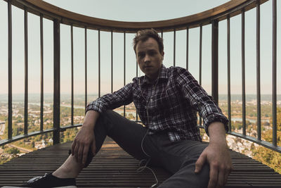 Portrait of young man sitting at observation point against sky