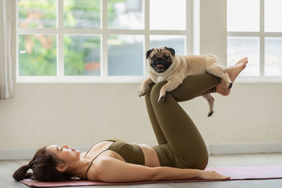 Full length of woman lying on exercise mat with dog at home