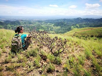 Rear view of man sitting on landscape against sky