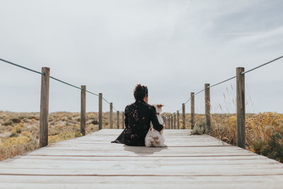 Woman sitting on railing against sky