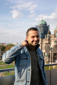 Portrait of man in denim jacket standing against buildings