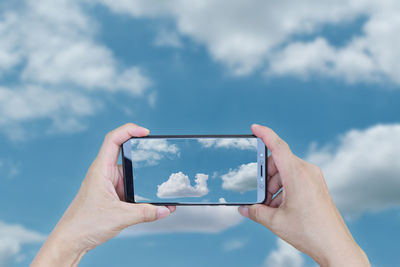 Cropped image of hand holding smart phone against sky