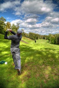 Rear view of man playing golf on playing field against sky