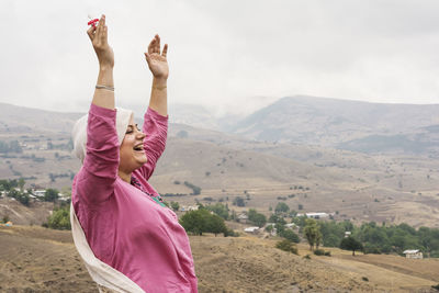  woman standing with arms raised against mountains