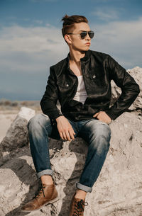 Full length of young man sitting on rock against sky