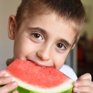 Close-up portrait of boy eating melon at home