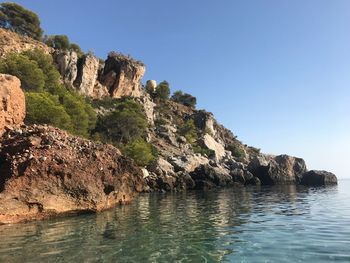 Rock formation by sea against clear blue sky