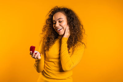 Portrait of a smiling young woman using phone against yellow background