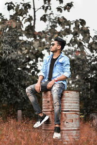 Young man sitting on barrel against trees