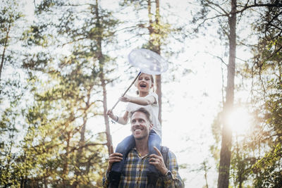Smiling father carrying happy daughter on shoulder while walking in forest