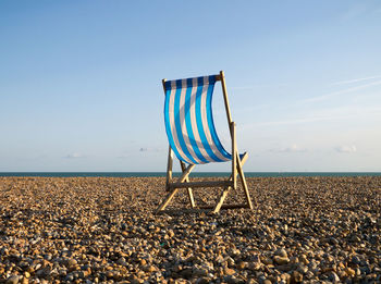 Deck chairs on shore at beach against sky