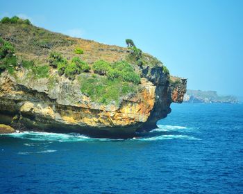 Scenic view of cliff by sea against clear blue sky