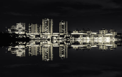 Illuminated buildings by river against sky at night