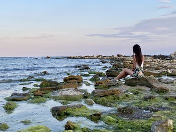 Woman on rocks at beach against sky