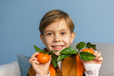 Portrait of a happy little boy holding freshly picked tangerines on a blue background.