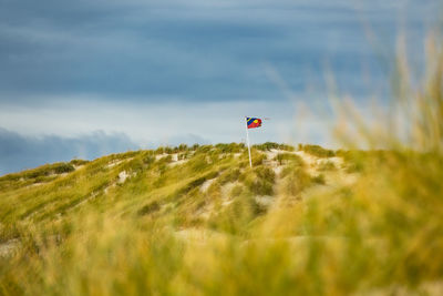 Mid distance view of flag on grassy hill against cloudy sky