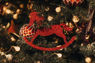 Vintage toy in the form of a red shiny horse hanging on the christmas tree. festive background. 