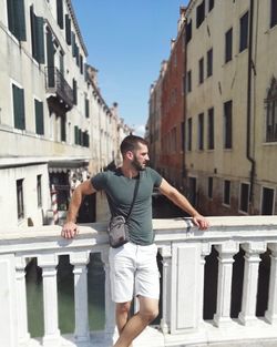 Young man standing by railing against buildings