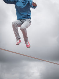 Low section of man jumping over rope against cloudy sky