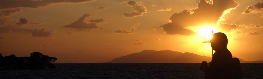 Silhouette person on sea against sky during sunset