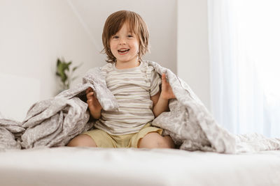 A boy of 4 years old jumps and indulges on the bed and wraps himself in a blanket. fun home games 