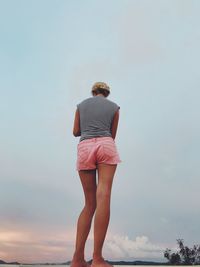Rear view of woman standing against cloudy sky during sunset