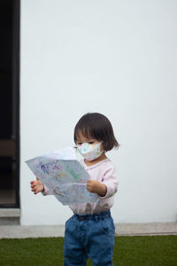 Baby girl holding paper and standing against wall