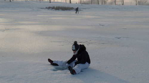 Boy bending while sitting on snow covered field