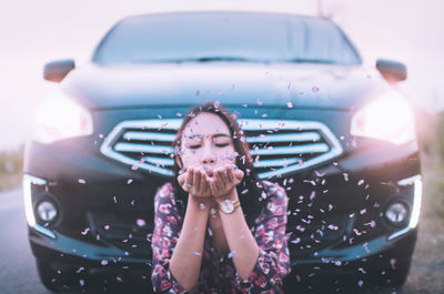 Close-up of young woman blowing petals against car