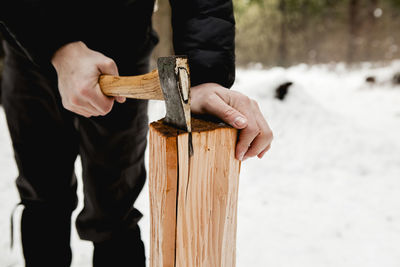 Midsection of man cutting wood in snow covered forest