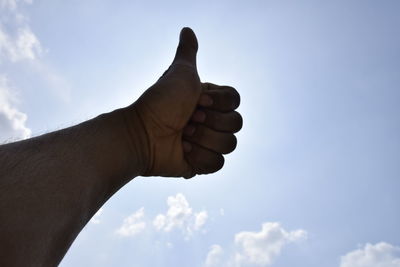 Cropped hand showing thumbs up against sky