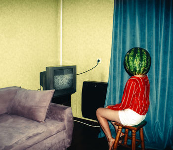 Young woman wearing watermelon on head sitting at home