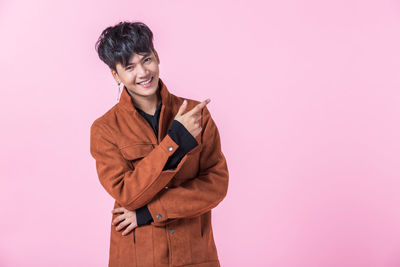 Smiling young woman standing against pink background