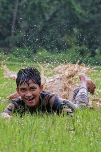 Cheerful young man lying on puddle amidst grassy land