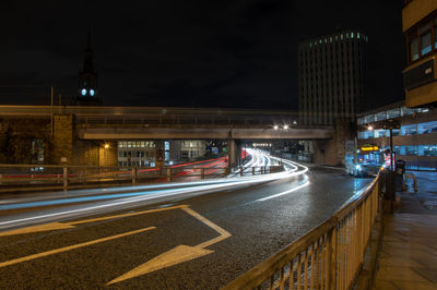 Light trails on road by illuminated buildings in city at night